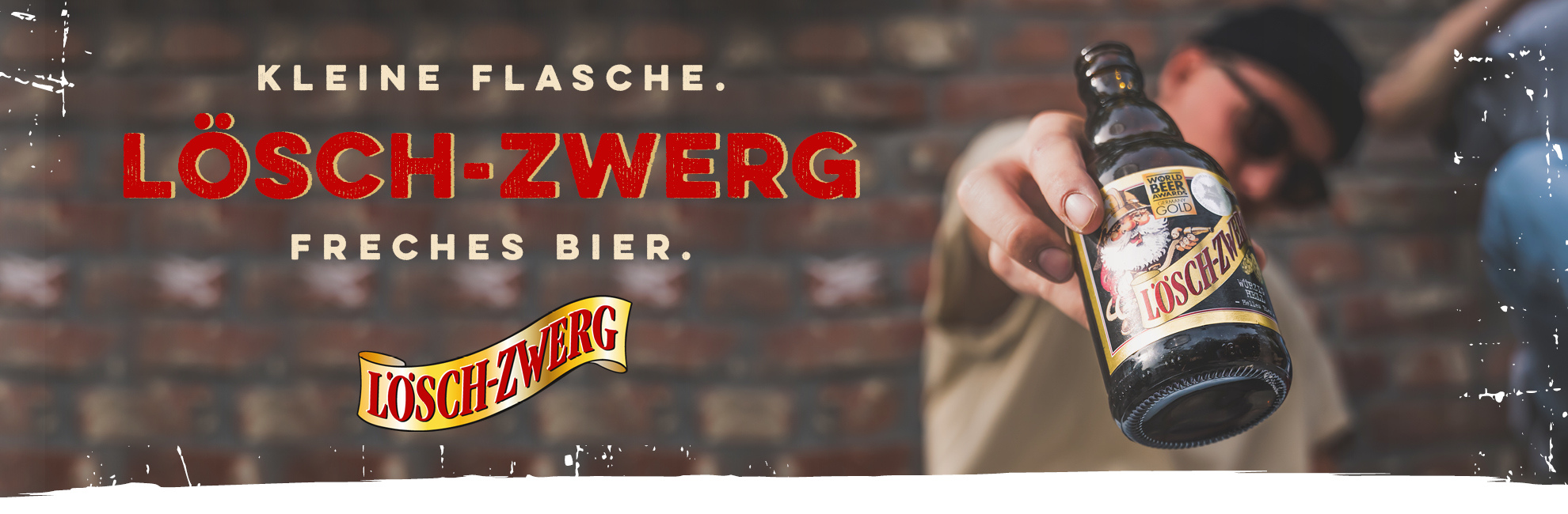 Werbebild für Lösch-Zwerg Bier: Im Vordergrund eine Hand mit einer kleinen Bierflasche der Marke Lösch-Zwerg, die zur Kamera gehalten wird. Im Hintergrund eine Backsteinwand und eine Person mit Sonnenbrille und Mütze. Der Slogan lautet: "Kleine Flasche. Lösch-Zwerg. Freches Bier."