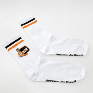 Ein Paar weiße Sportsocken mit schwarzen und orangefarbenen Streifen am gerippten Bündchen. An der Seite ist das Bazi-Logo mit Zitronenscheibe eingestickt, auf der Fußsohle steht der Schriftzug "Servus, du Bazi!"