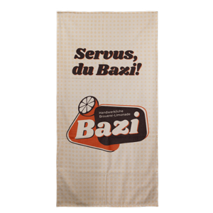 Großes Strandtuch. Cremefarben mit dunkleren Punkten. Großer Schriftzug "Servus, du Bazi!". Darunter befindet sich das Bazi Cola-Mix Logo.